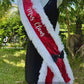 Add a festive touch to your holiday look with this vibrant red sequin “Mrs. Claus” sash! Trimmed in soft, white faux fur for a cozy, wintery feel, this sash catches the light with every step. A chic black satin bow with a gold accent adds a pop of elegance, completing the classic Christmas-inspired design.